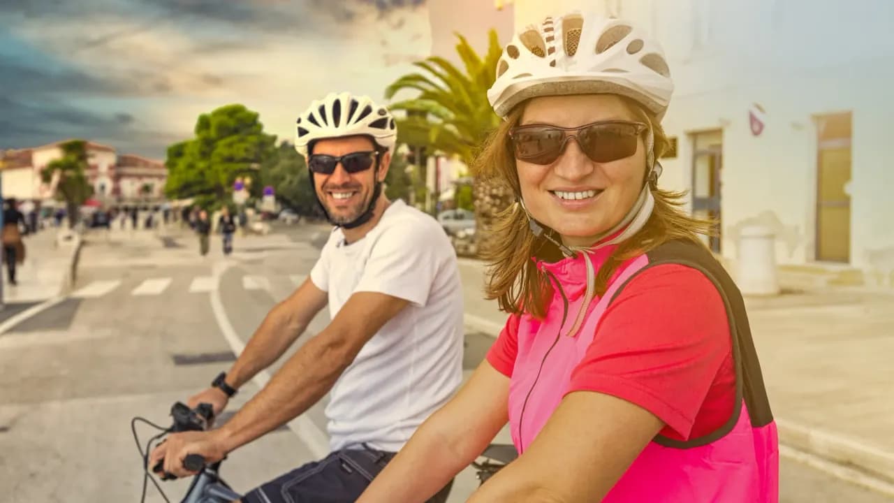 Individuelle Radreise auf Mallorca: lachendes Paar mit Helmen auf dem Rad in einem Dorf