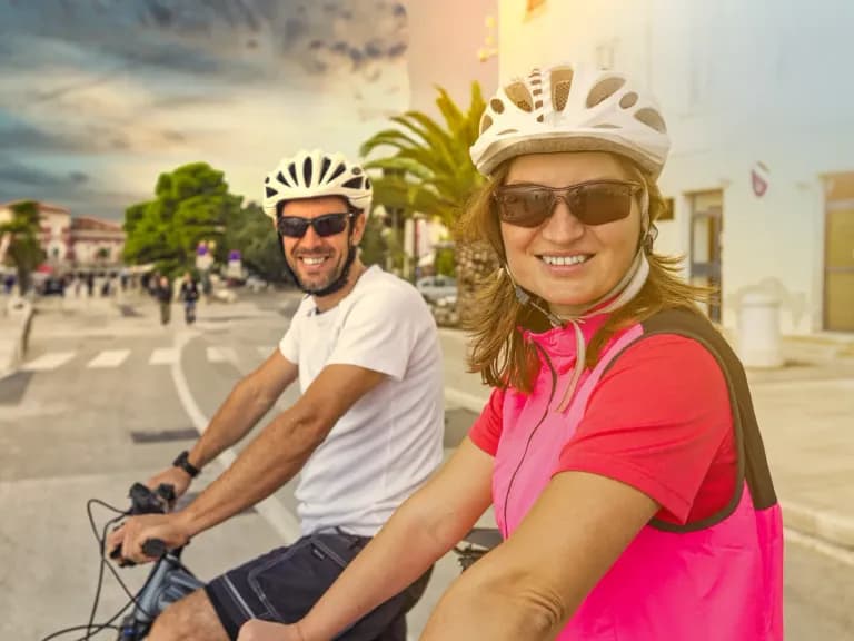 Individuelle Radreise auf Mallorca: lachendes Paar mit Helmen auf dem Rad in einem Dorf
